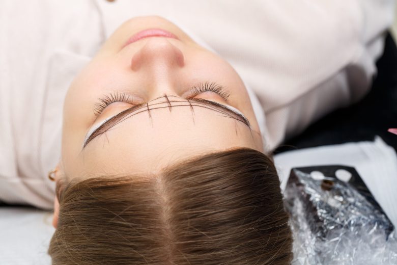 Beautician tattooing a woman's eyebrows using special equipment during permanent make-up, close-up.