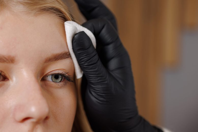 Master eyebrowist makes eyebrow correction to a girl in a beauty salon, close-up